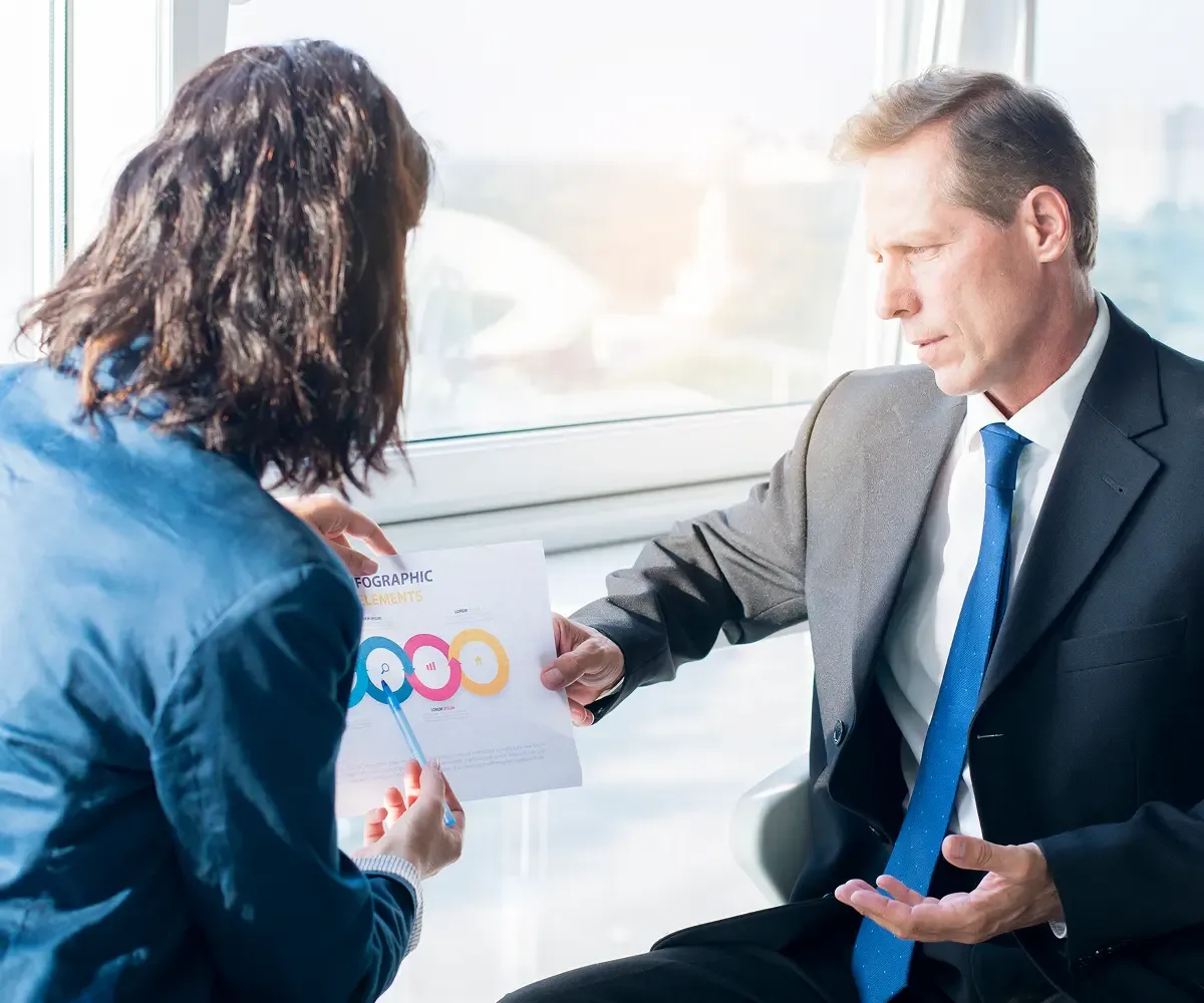 businesswoman-explaining-infographic-elements-sheet-her-male-partner 1